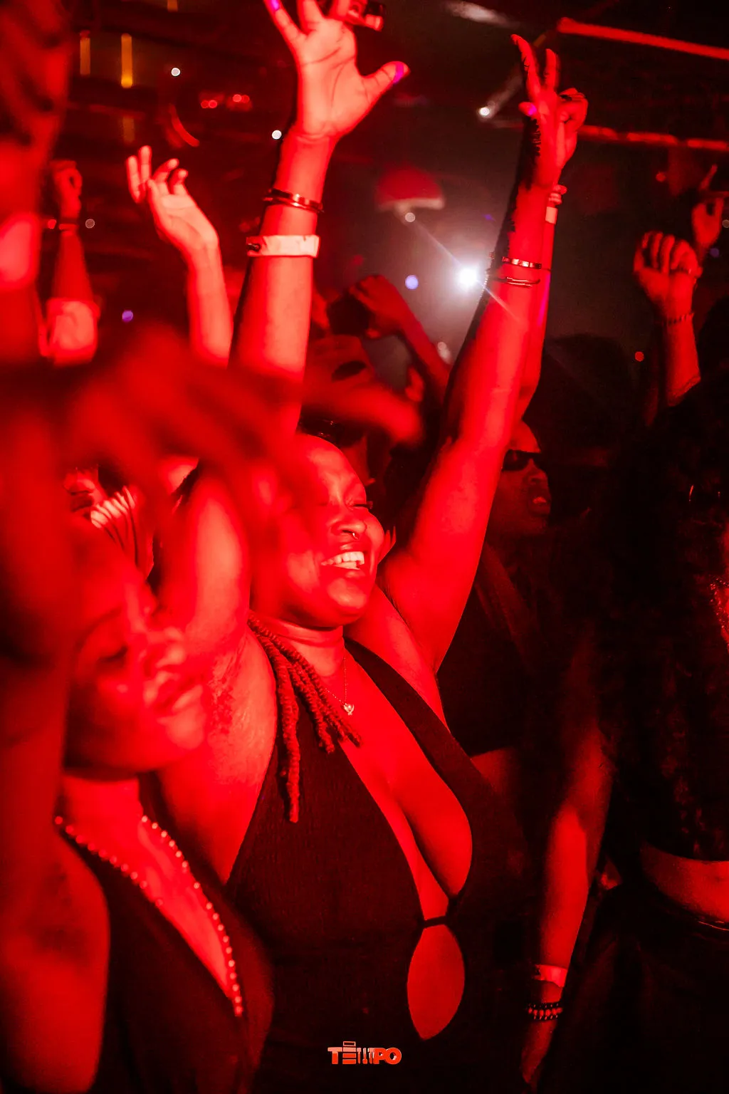 Hands in the air across a red-lit dance floor