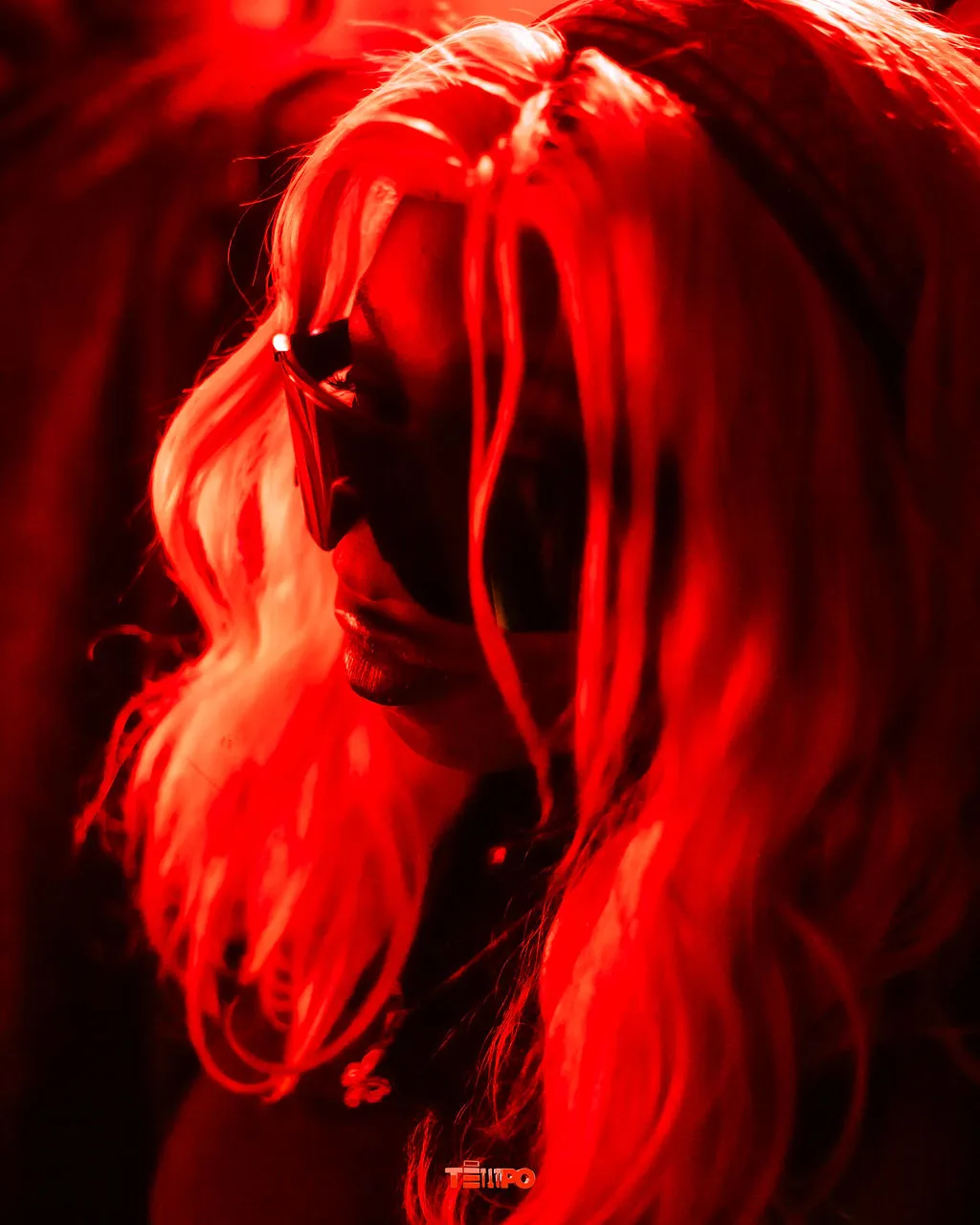 A raver lit in deep red, hair falling across her face